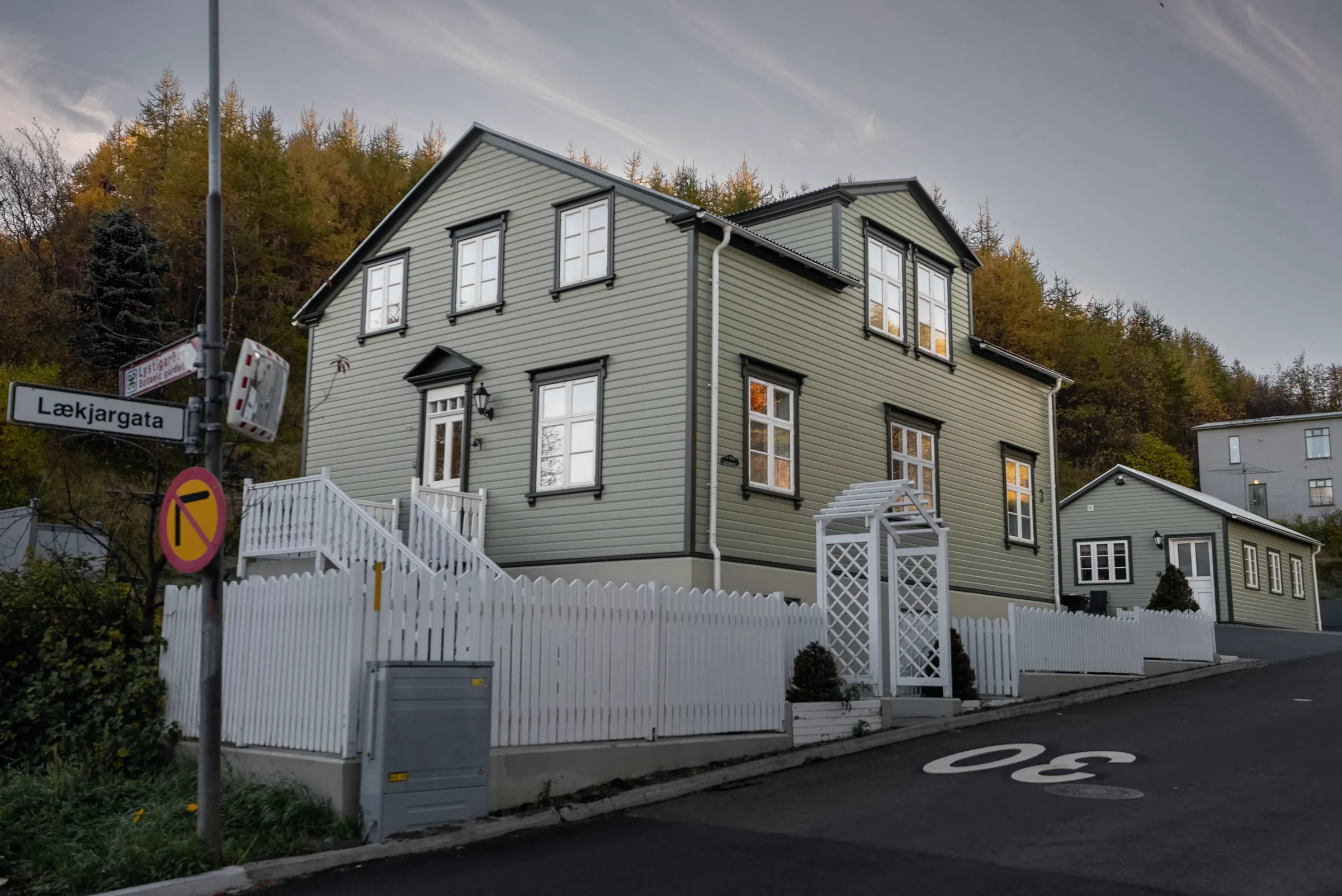 The house at Lækjargata 3 seen from the street corner, pale green with white trim, a white fence and the road below